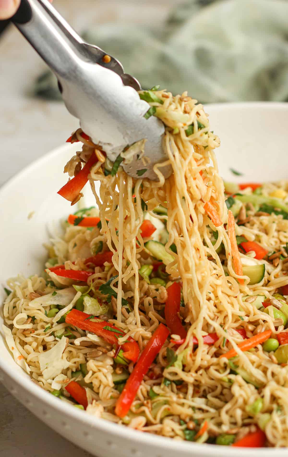 A salad tongs lifting some of the ramen salad out of the bowl.