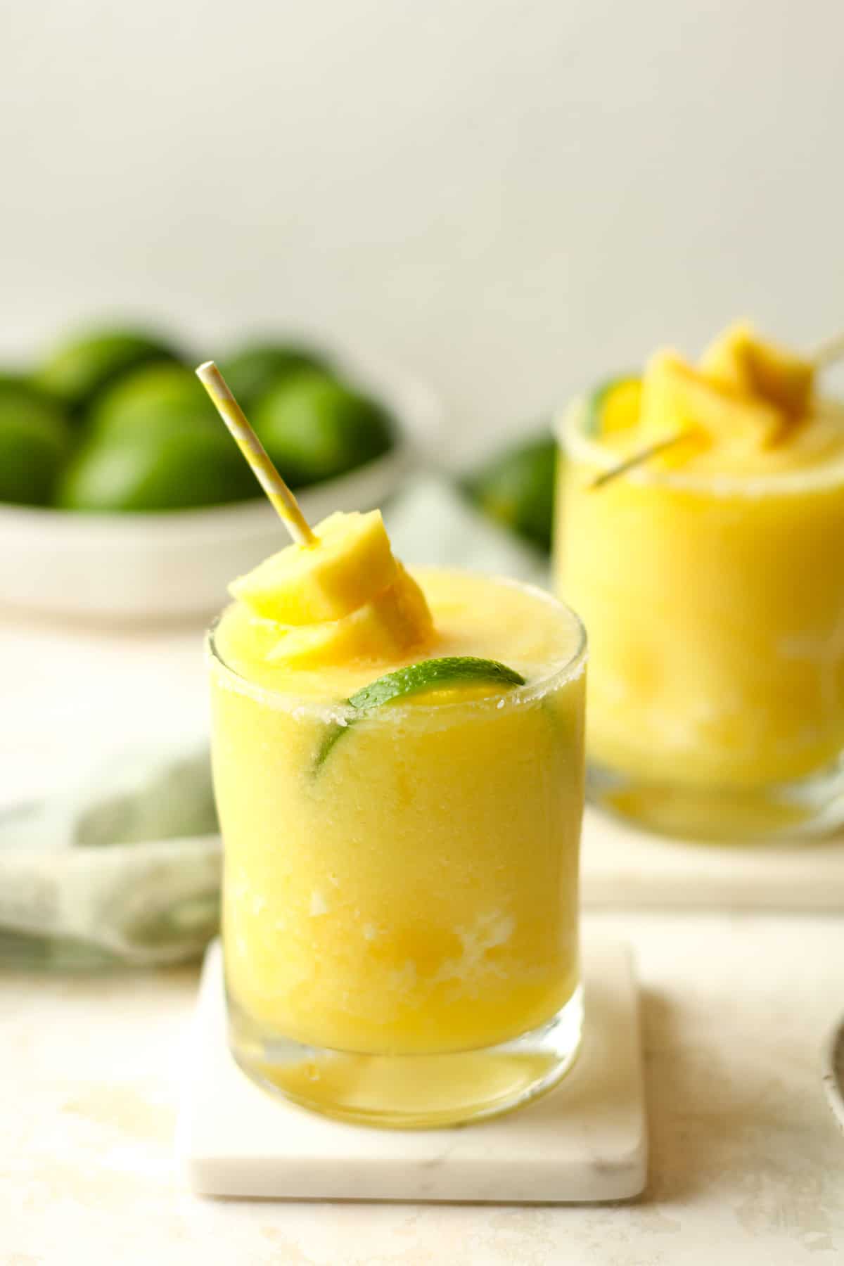 Side view of two frozen margaritas with limes.