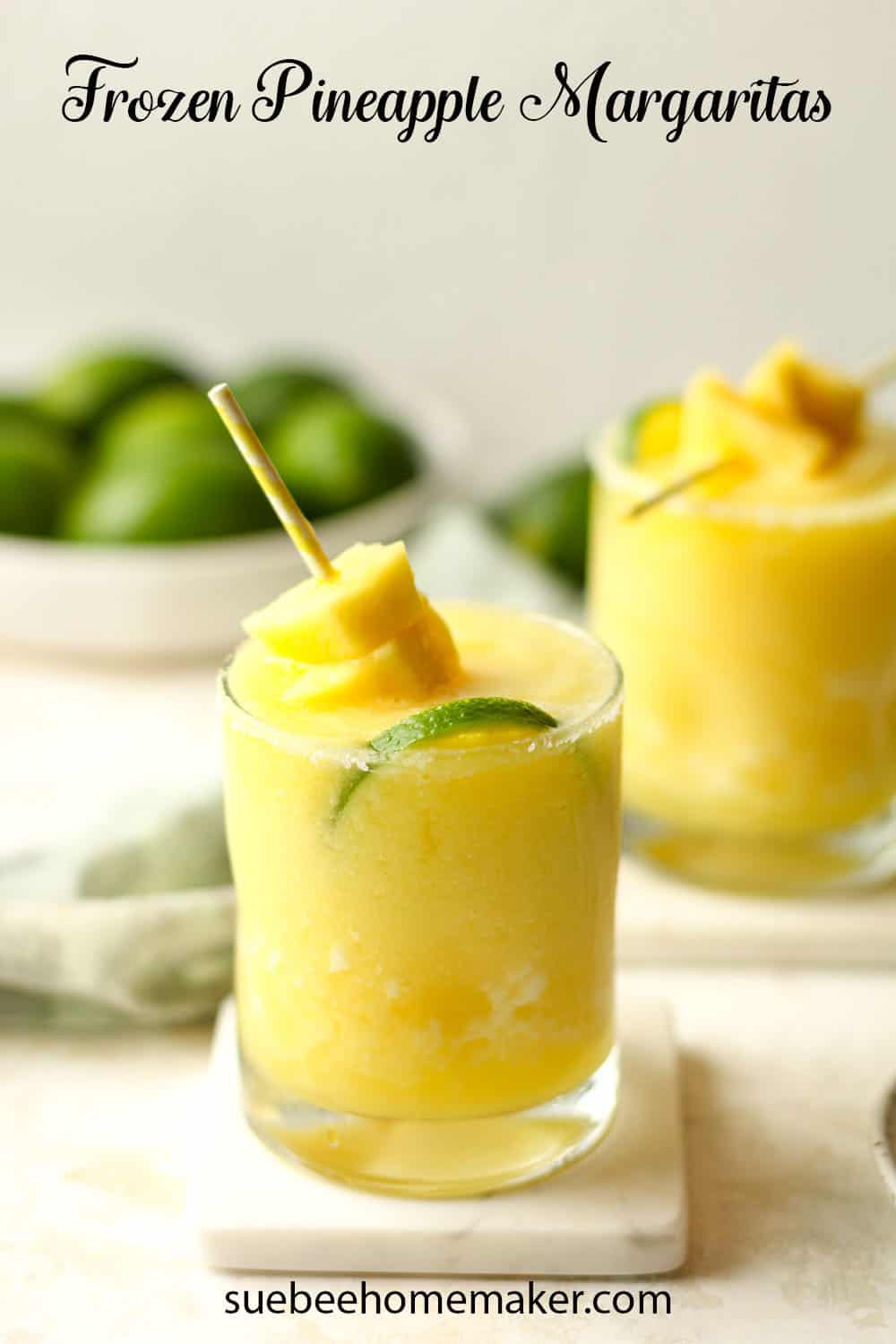 Side view of two glasses of pineapple margaritas with a pineapple garnish and a slice of lime.