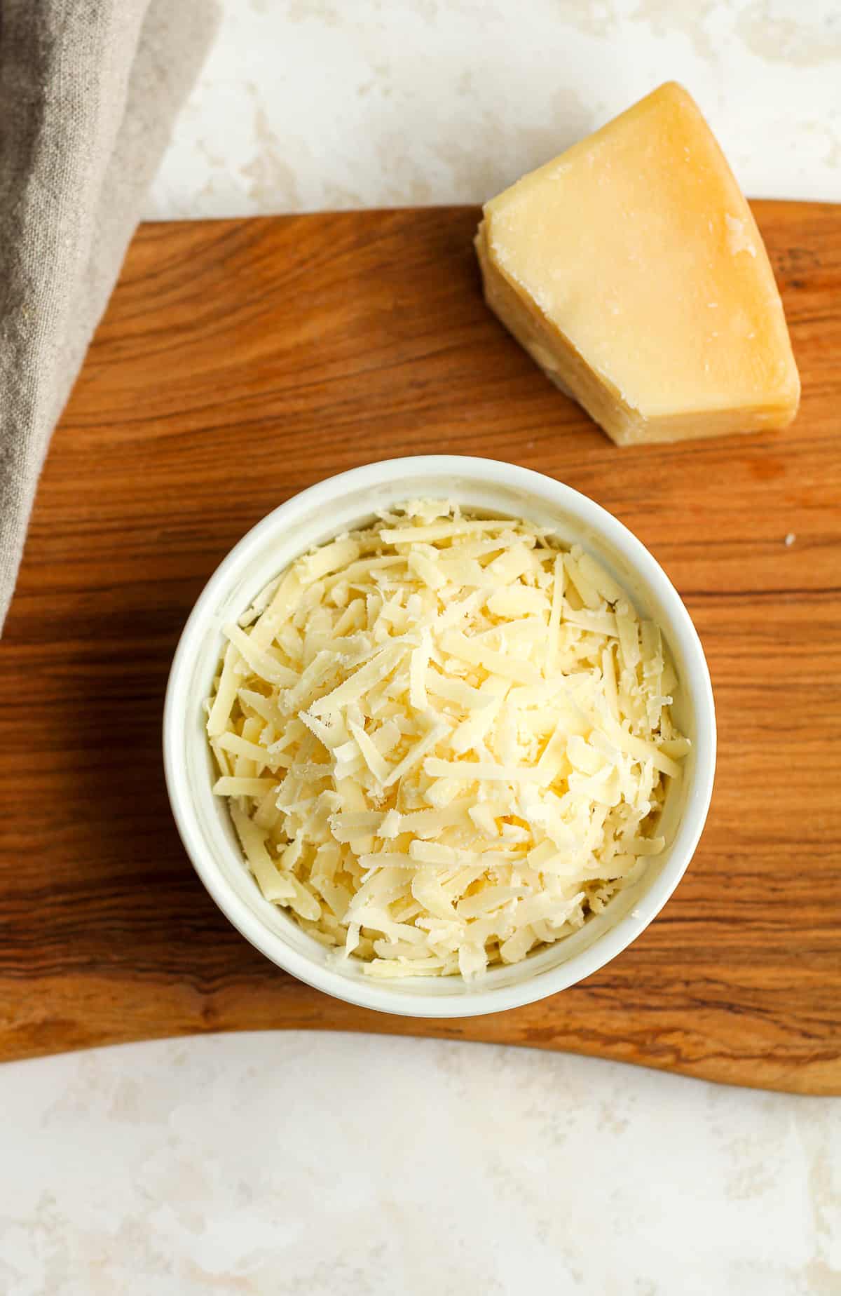 A bowl of shredded parmesan cheese, with a partial chunk next to it.