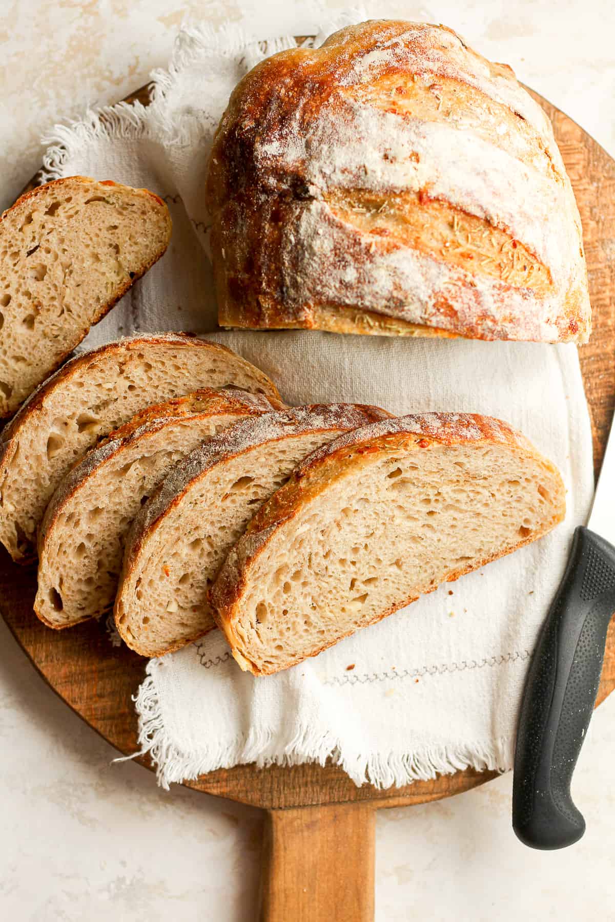 A round board with some sliced sourdough and a partial loaf, with a knife.