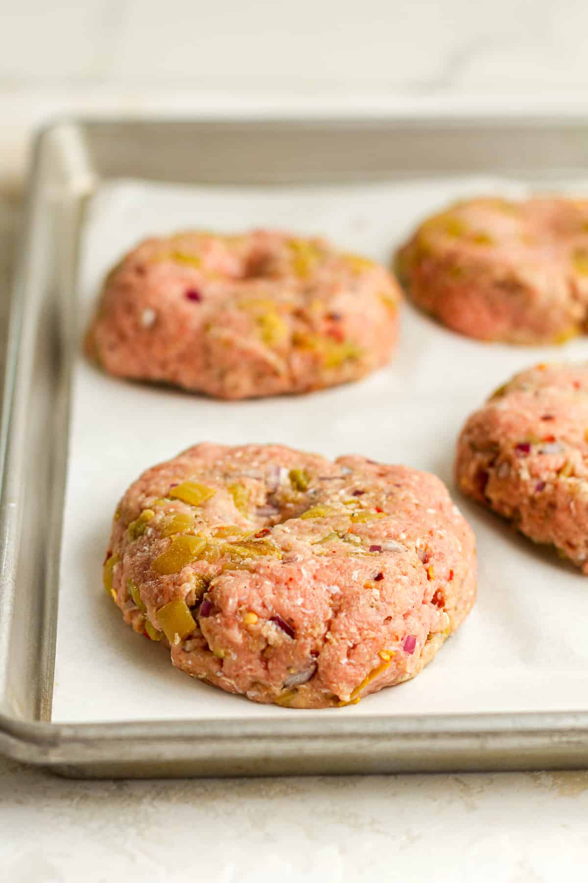 Side view of four raw green Chile turkey burgers.