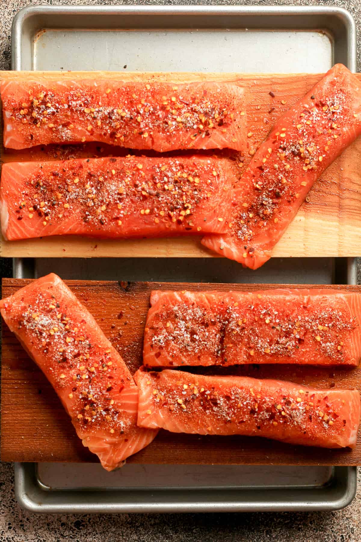The pan with the raw salmon with seasoning on two planks.