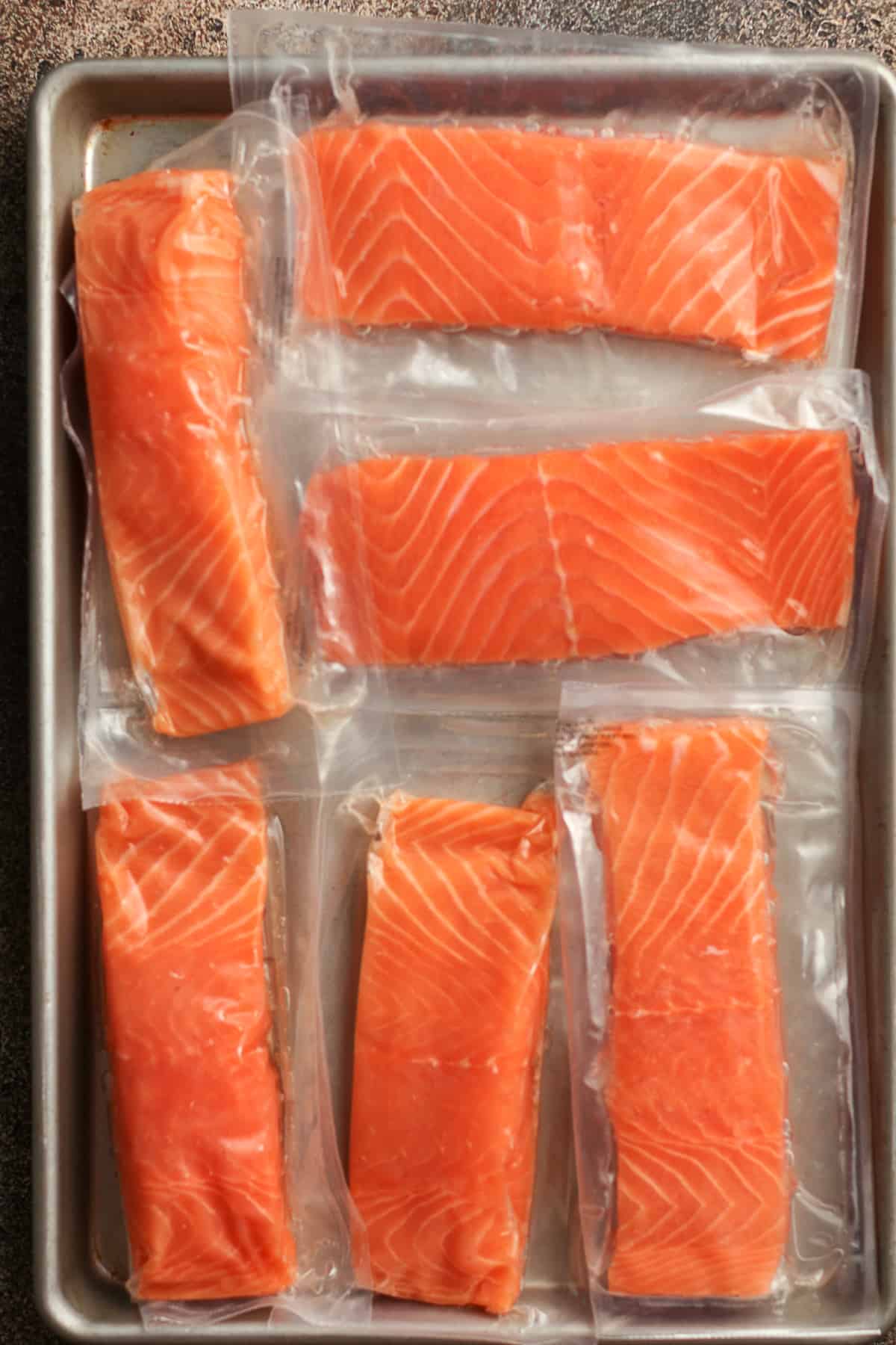 Six packaged pieces of salmon on a sheet pan.