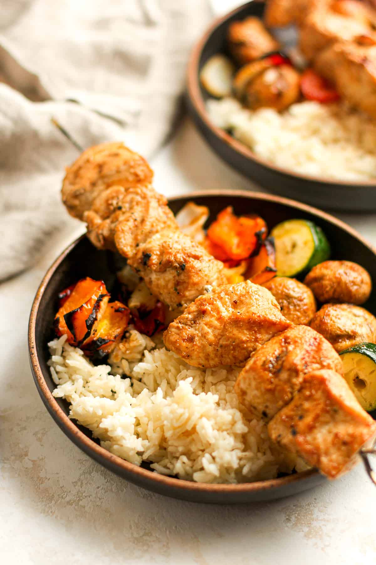 Side view of two bowls of rice, veggies, and skewered chicken.