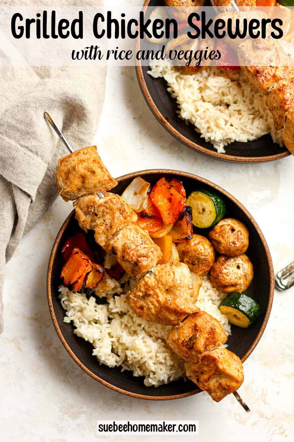 Two bowls of rice, grilled veggies, and chicken skewers.