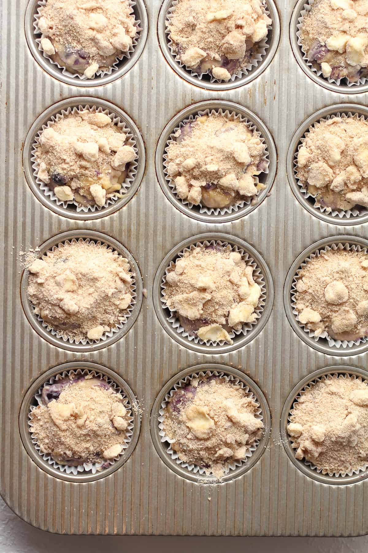 A muffin tin with the muffin dough and streusel topping ready to bake.