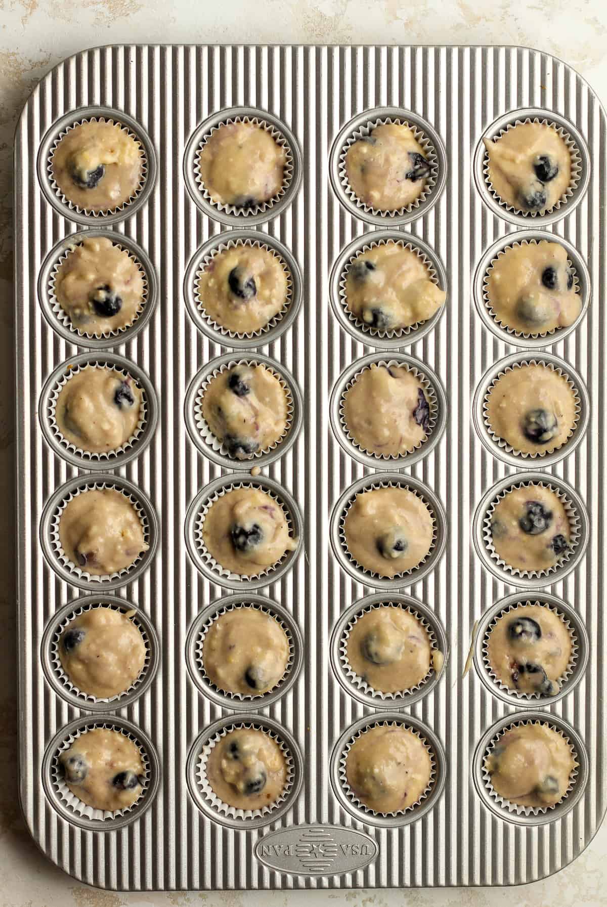 A mini muffin tin with blueberry batter.