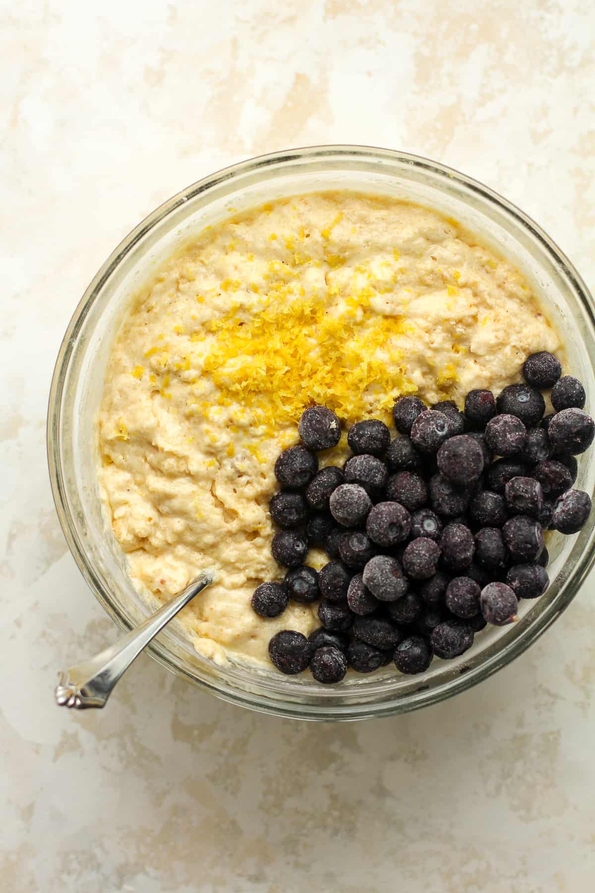 A bowl of the blueberry muffin batter with blueberries and lemon zest on top.