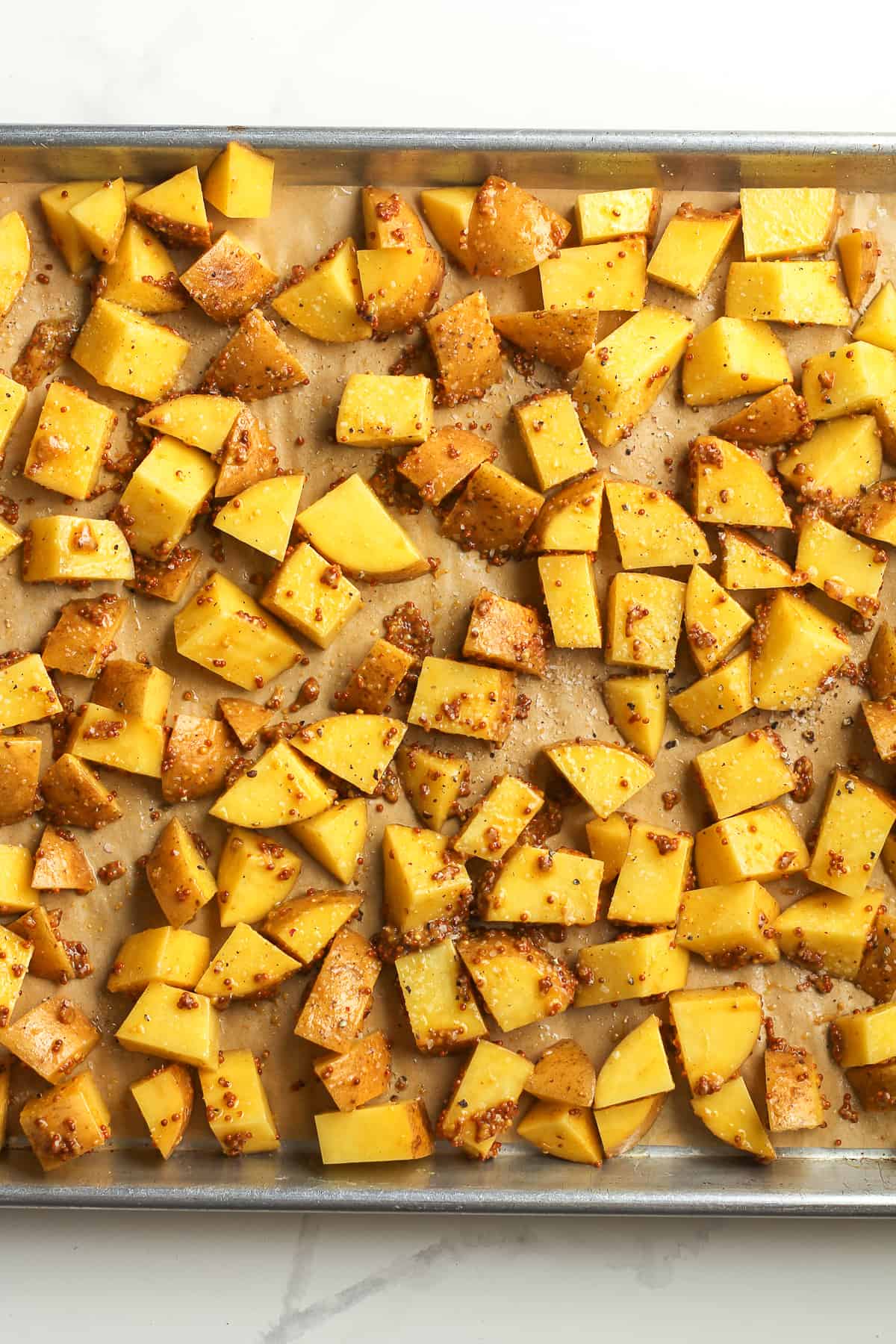 A pan of the chopped yellow potatoes with toppings before roasting.