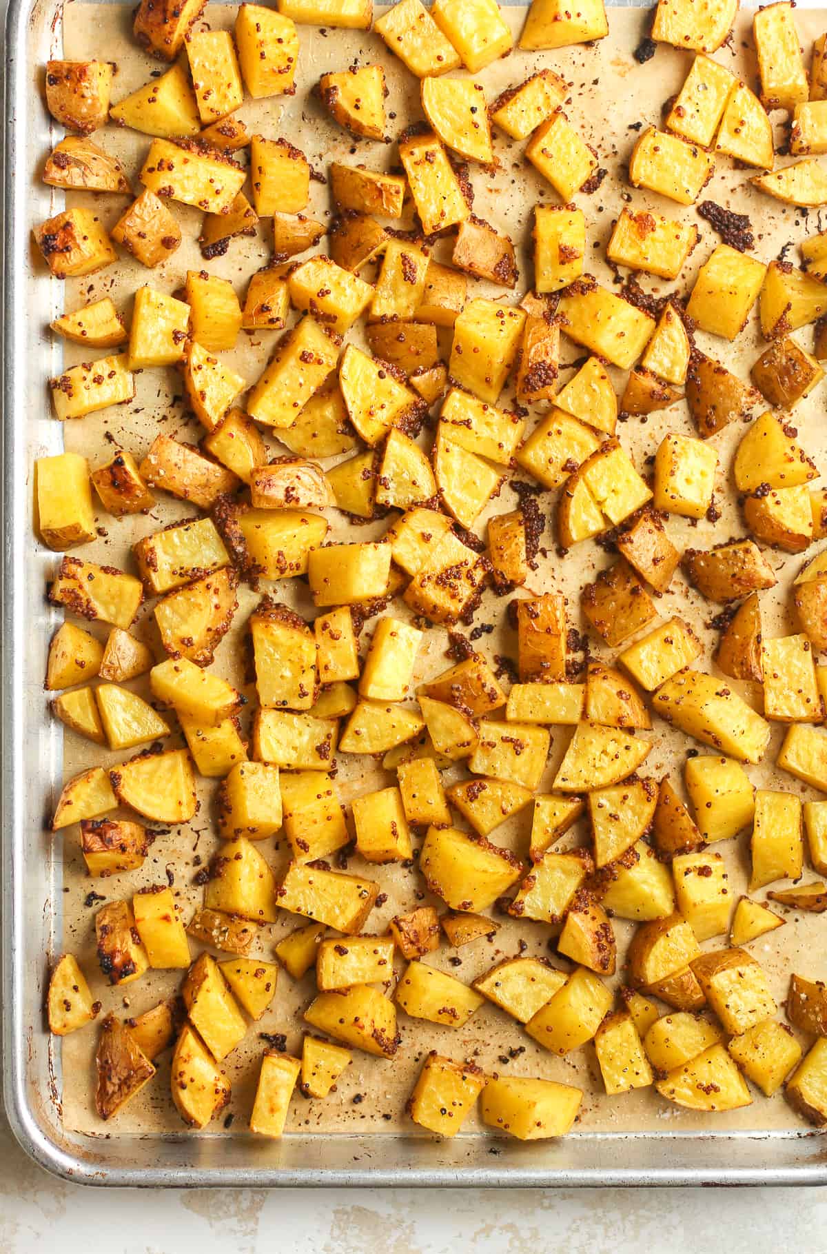 Overhead view of a large sheet pan full of mustard roasted potatoes.