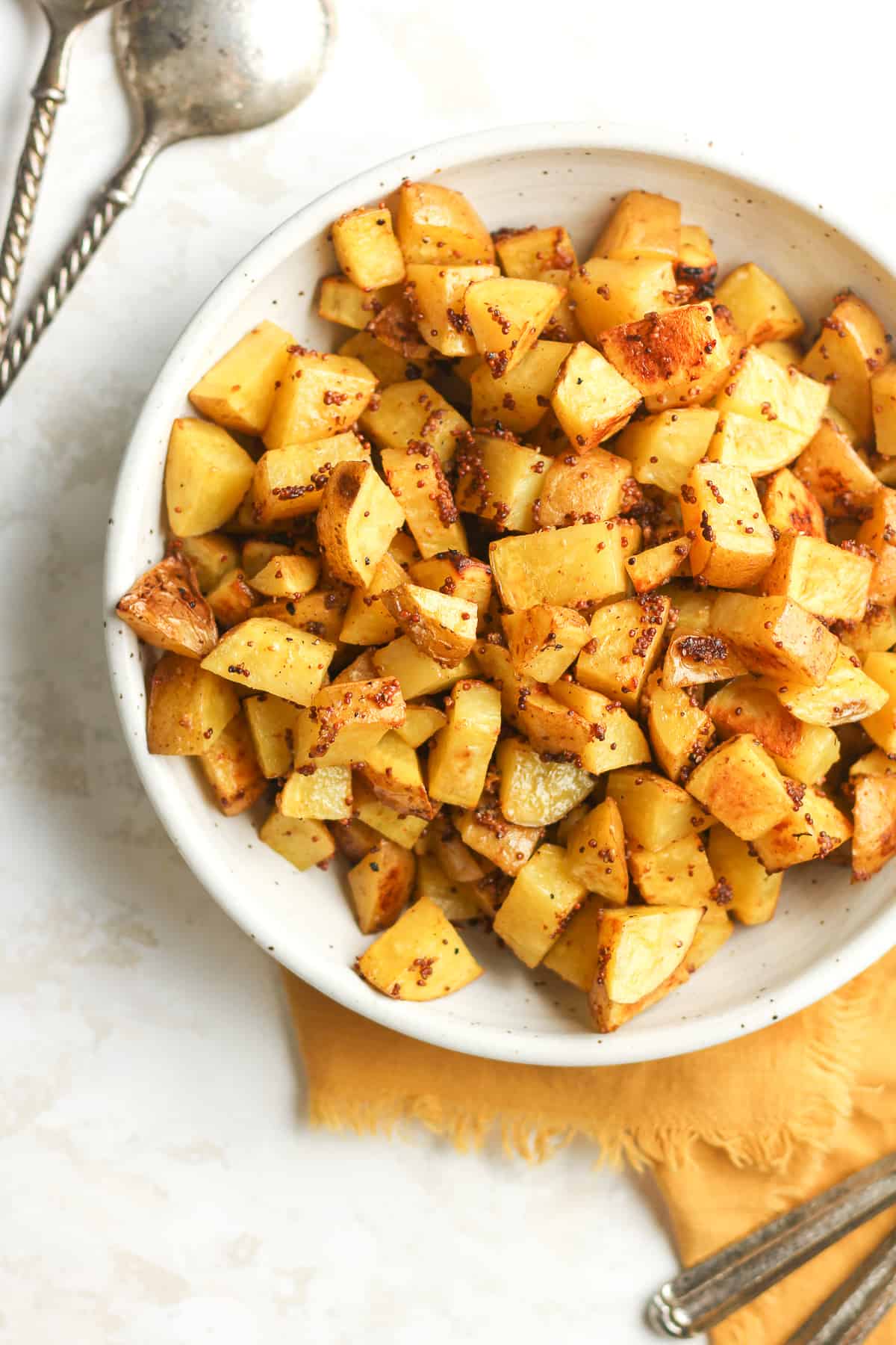 A large bowl of mustard roasted potatoes, with a gold napkin.