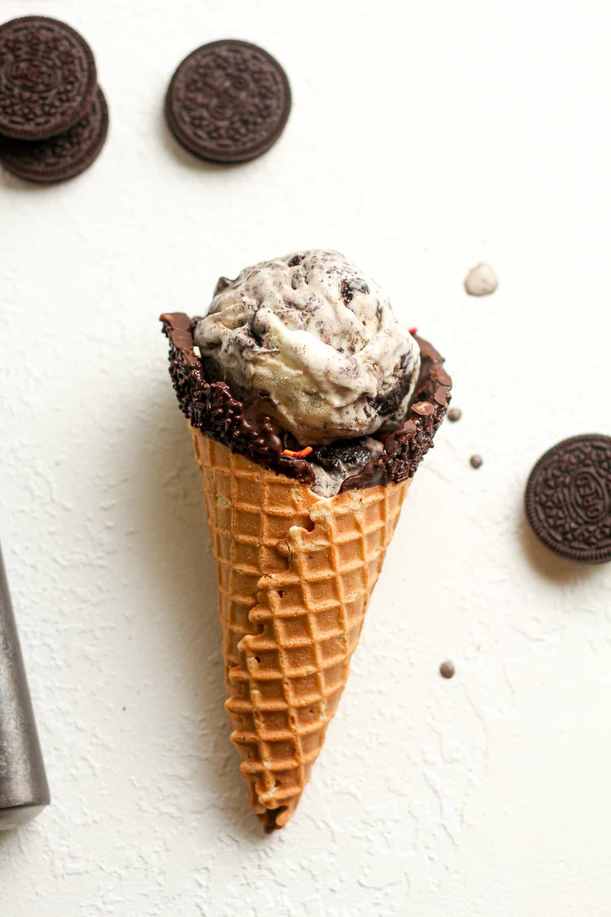 A waffle cone filled with cookies and cream ice cream, lying on a white surface.
