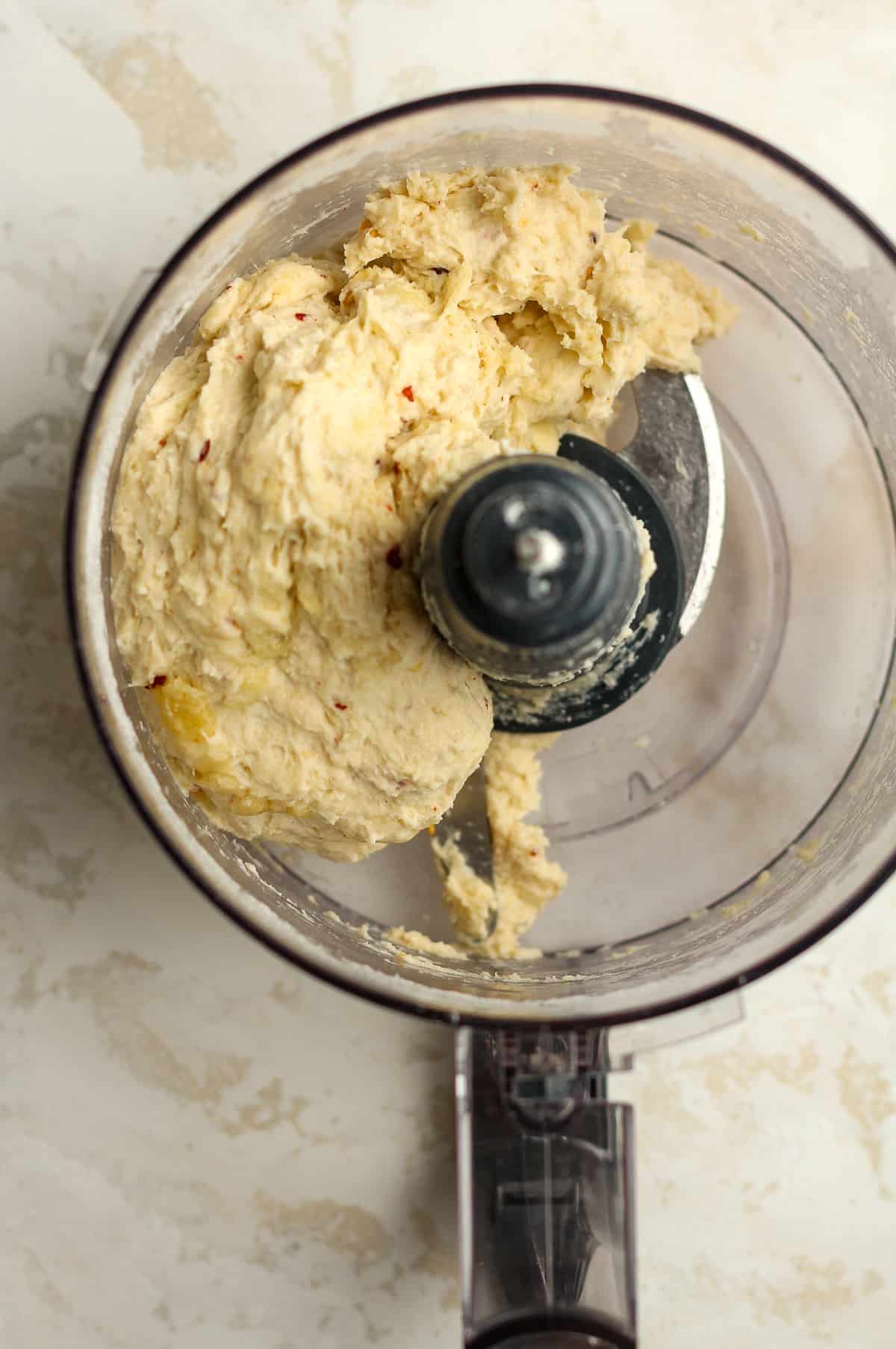 Closeup on the flatbread dough pushed to the side of the food processor.