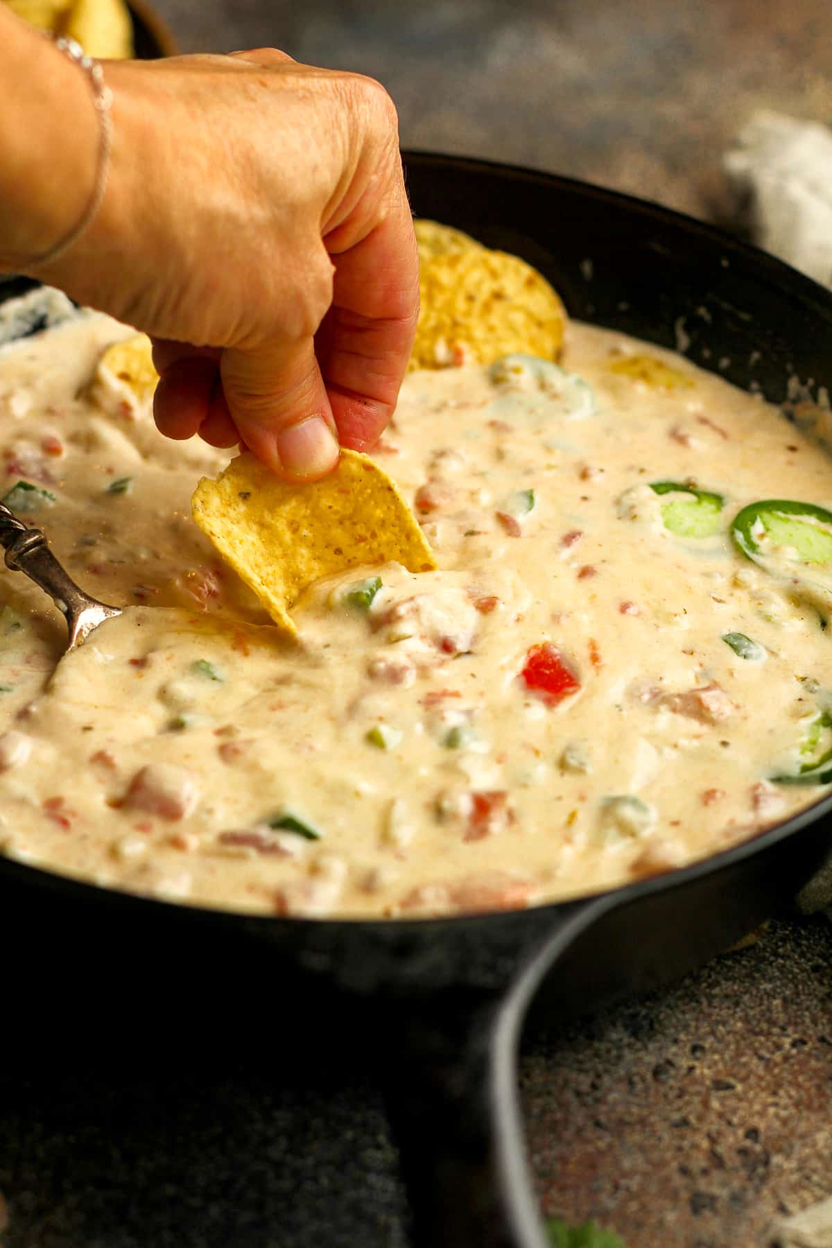 A hand dipping a chip into a pan of pepper jack queso.