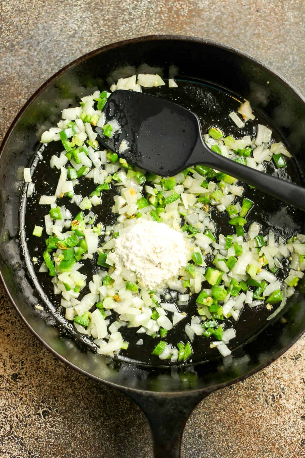 A skillet of the sautéed onions and jalapeños, with a tablespoon of flour on top.
