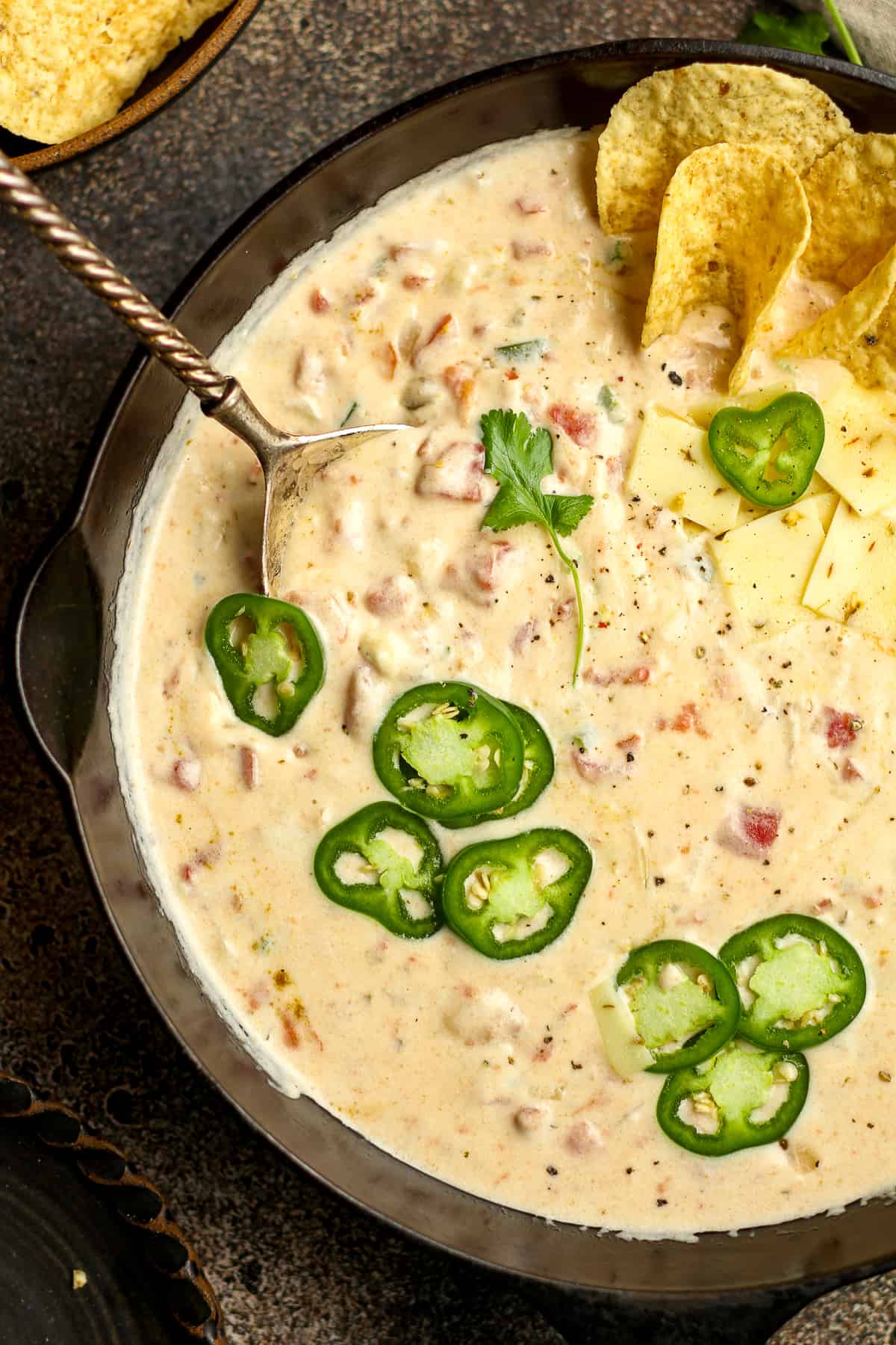 Closeup of a skillet of white queso with a spoon, topped with fresh sliced jalapeños.