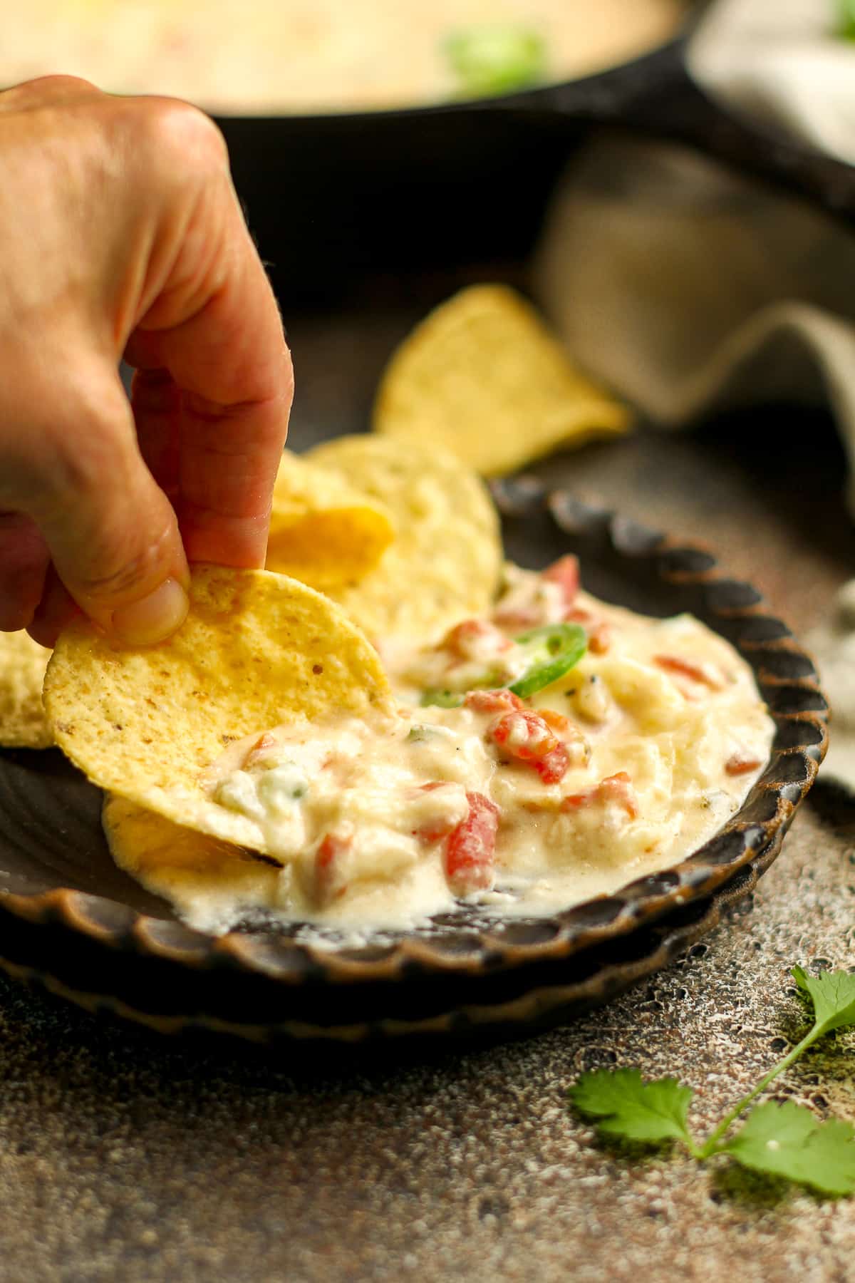 A hand dipping a chip into a small plate with queso and chips.