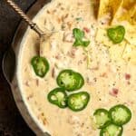 Closeup on a skillet of pepper jack queso, with fresh jalapeño slices and chips on top.