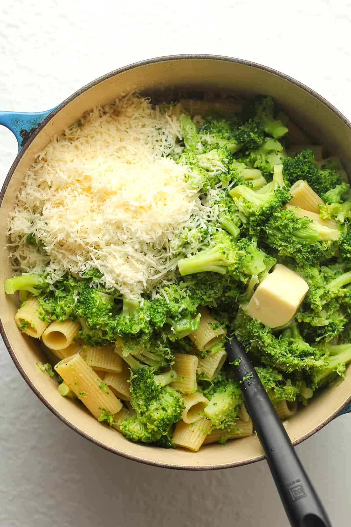 A stock pot of the pasta with broccoli and parmesan cheese on top.
