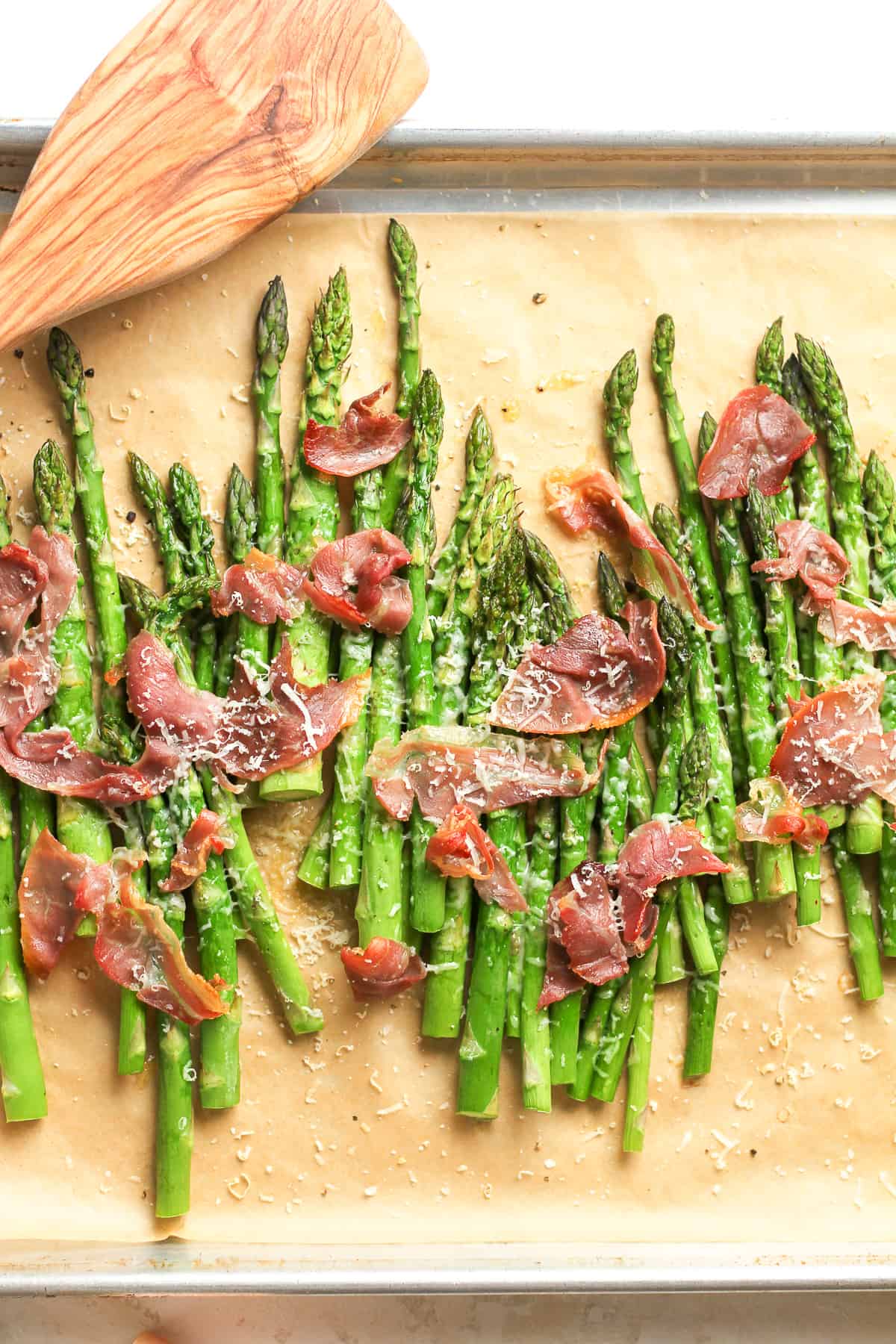 A sheet pan of the roasted asparagus with the torn prosciutto and shaved parmesan.