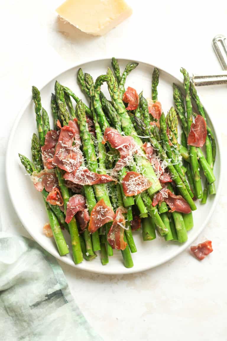 A white plate of the roasted asparagus with prosciutto and parmesan cheese.