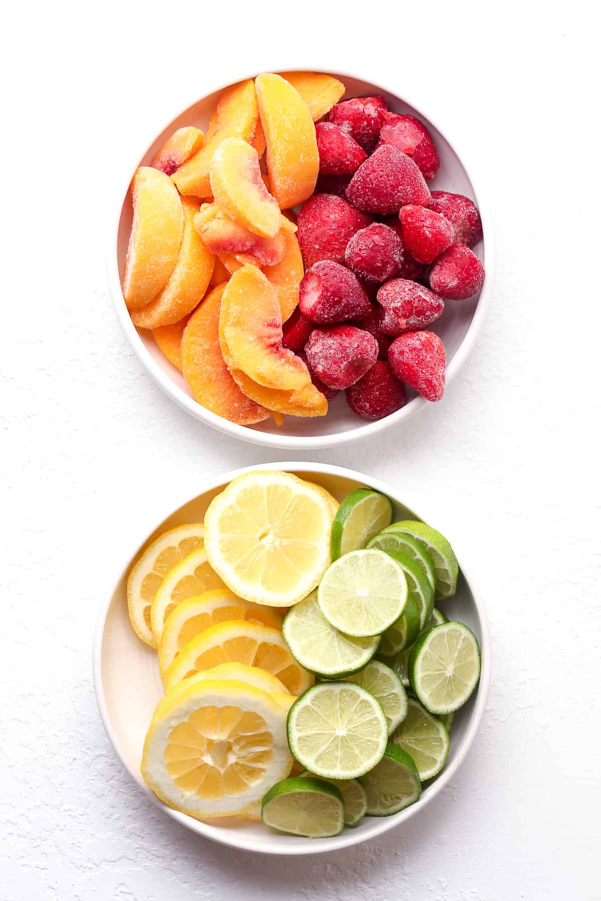 Two bowls of 1) frozen peaches and strawberries and 2) fresh lemon and lime slices.
