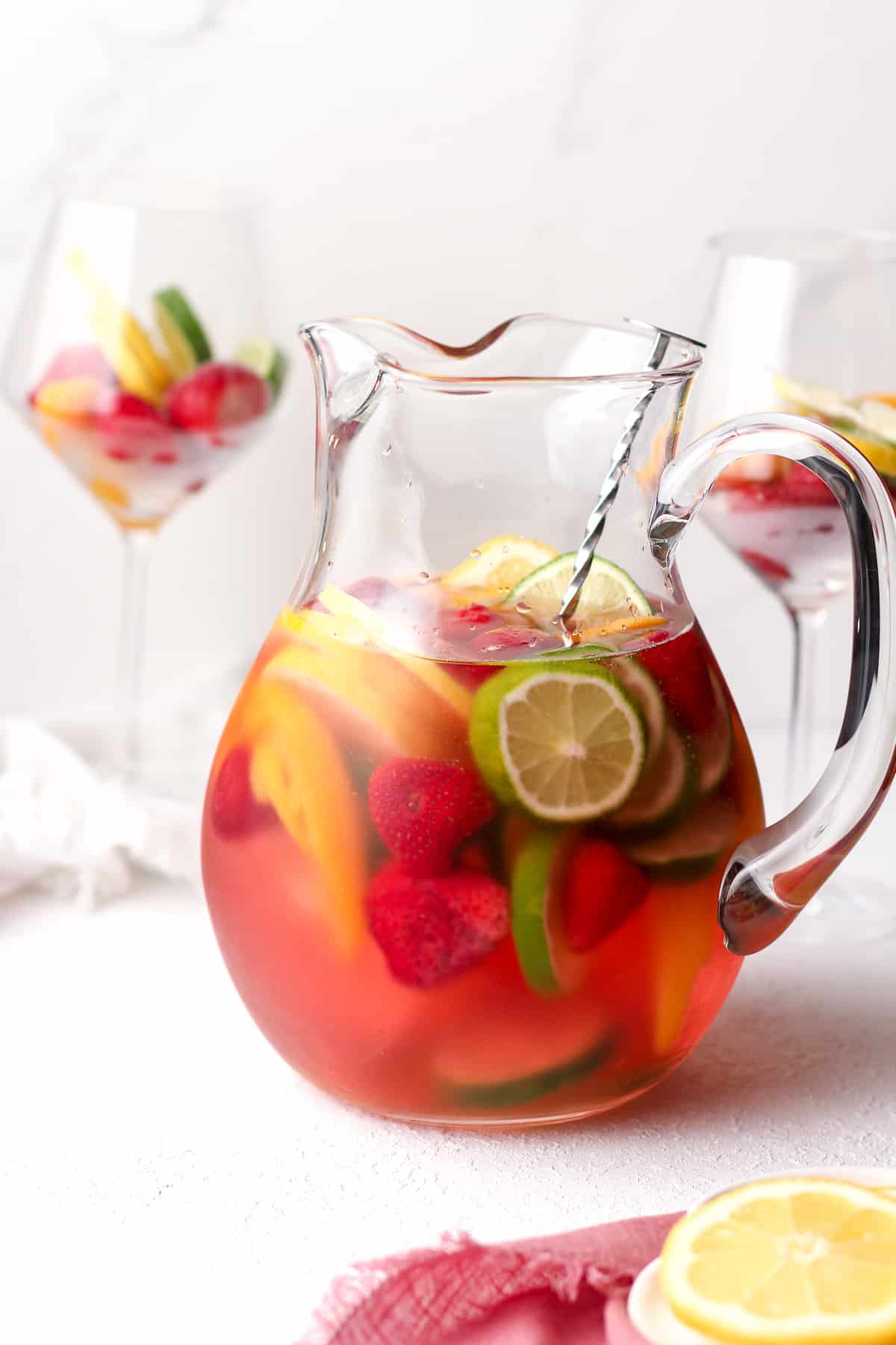 Side view of a pitcher of sangria, with sliced lemons, limes, and frozen strawberries.