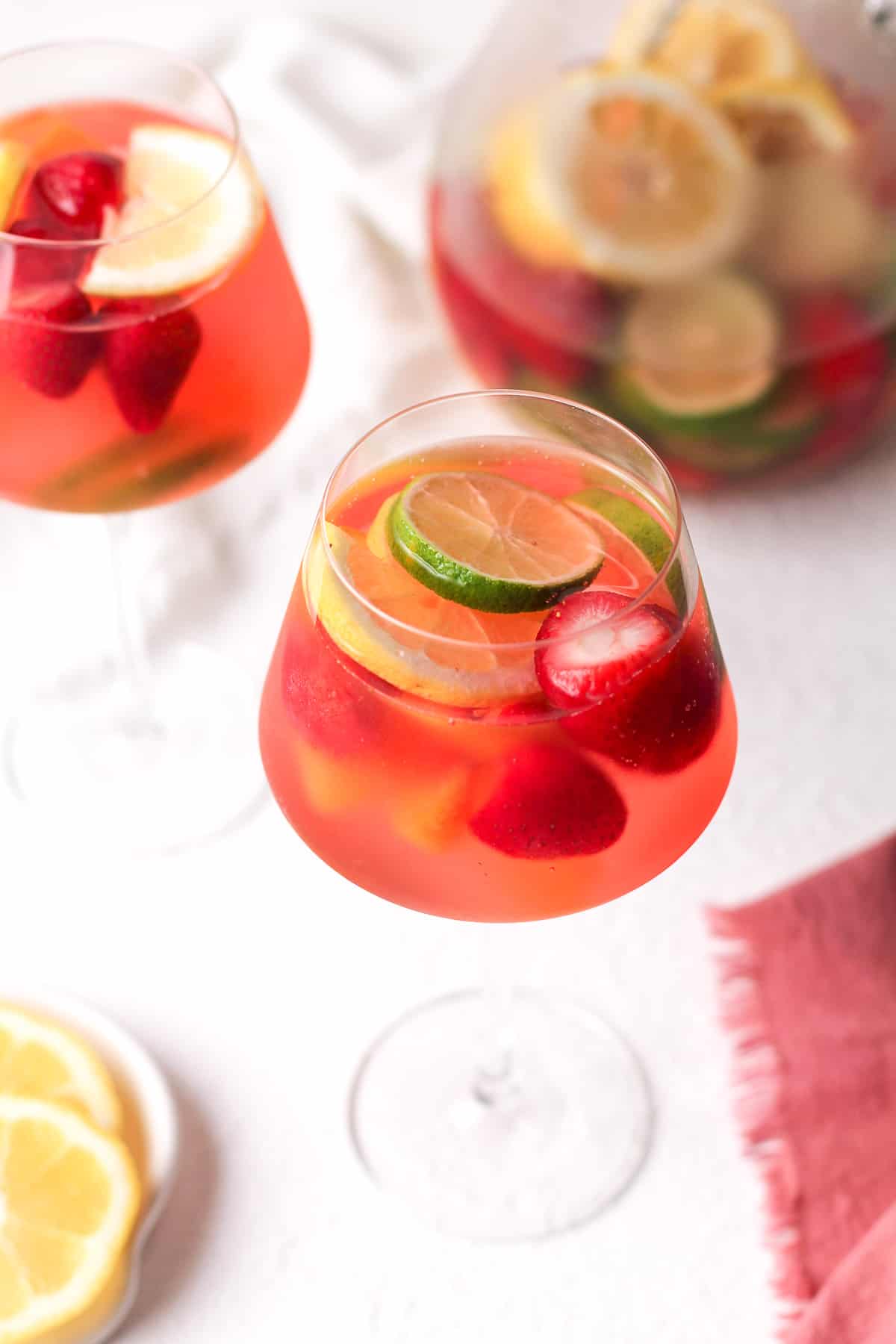 An overhead side angle of two glasses of rose sangria, with a pitcher in the background.