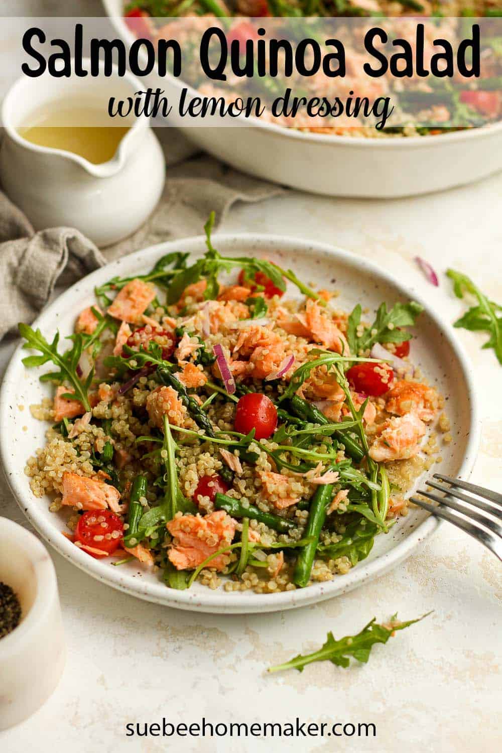 Side view of a plate of salmon quinoa salad, with a jar of lemon dressing.