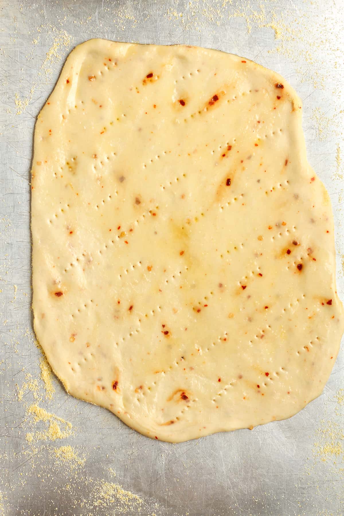 The flatbread dough rolled out with fork holes and olive oil on top.