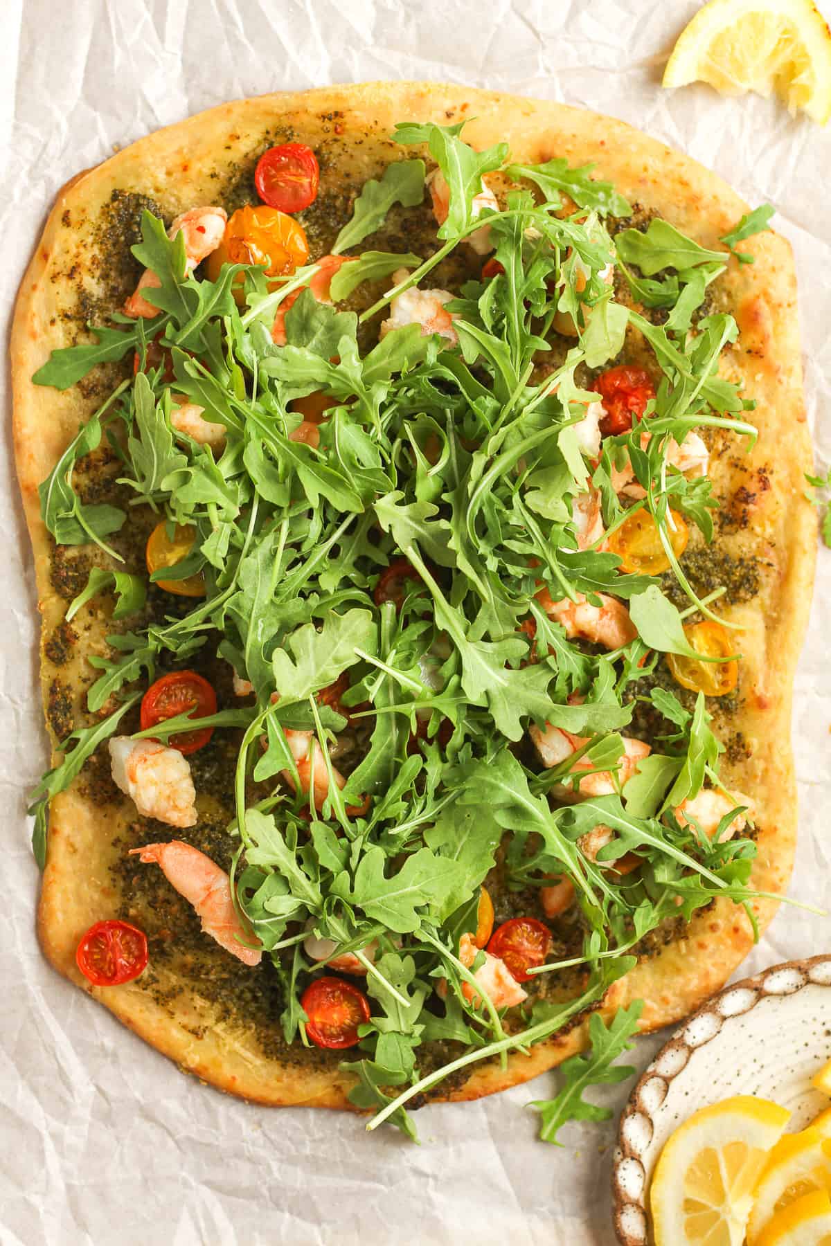 A whole shrimp pesto flatbread with arugula on top.