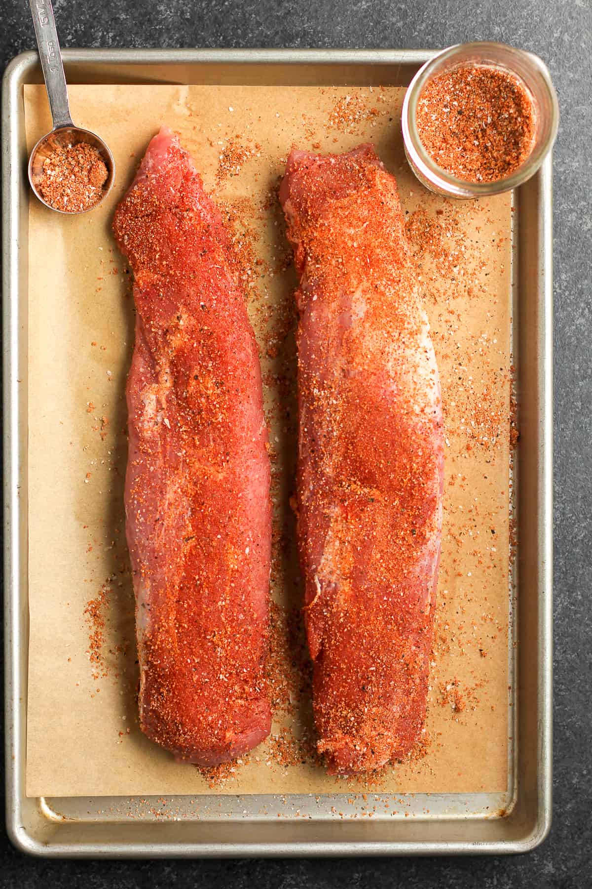 The baking sheet with the raw pork tenderloin topped with the dry rub seasoning.