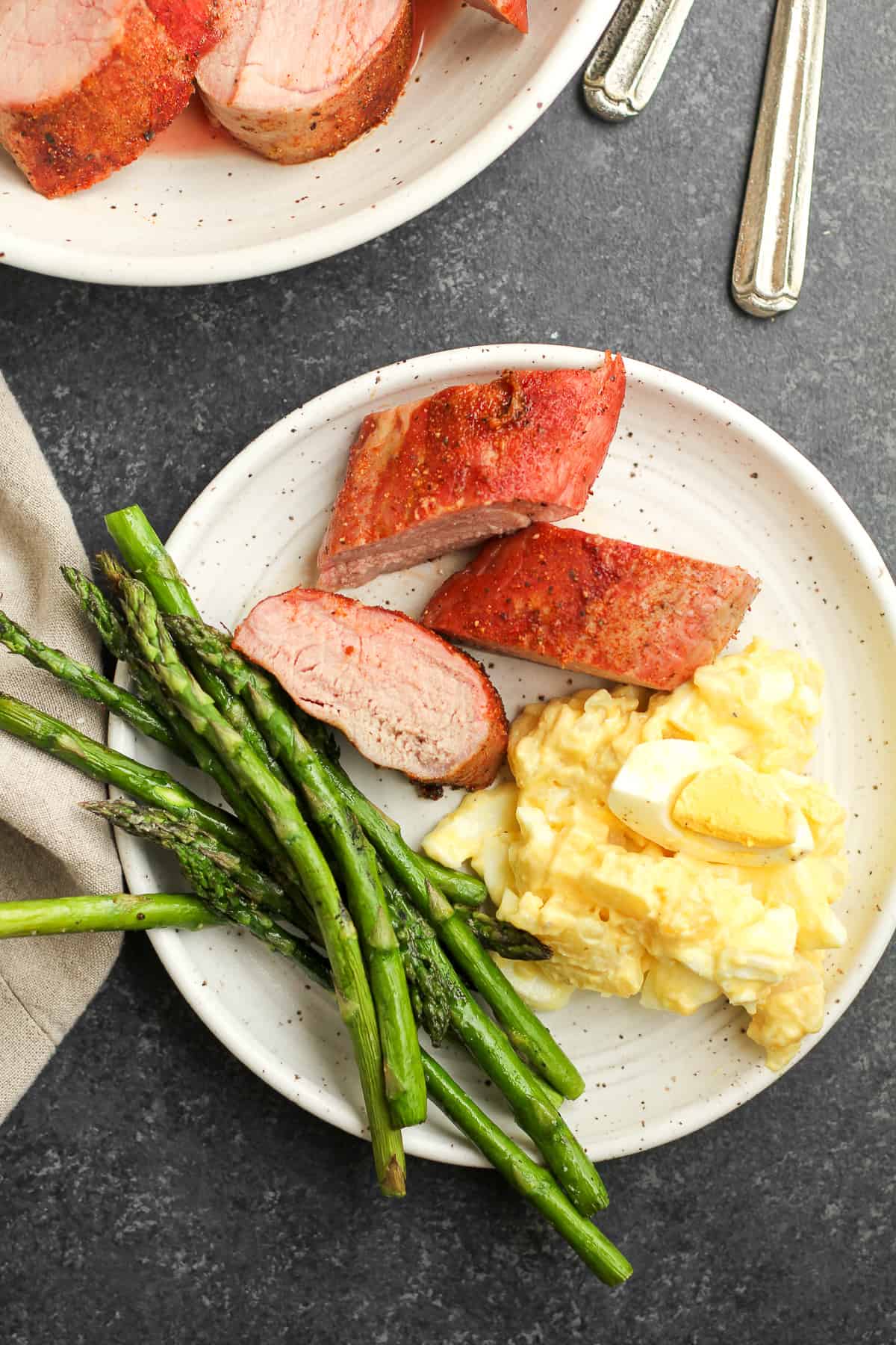 Overhead view of a plate of smoked pork tenderloin, potato salad, and grilled asparagus.