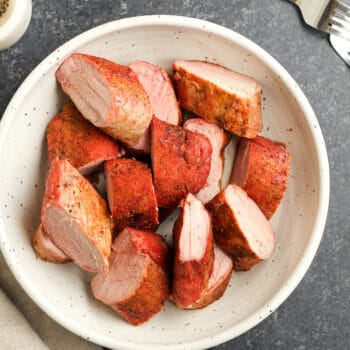 A white bowl of sliced pork tenderloin that has been smoked.