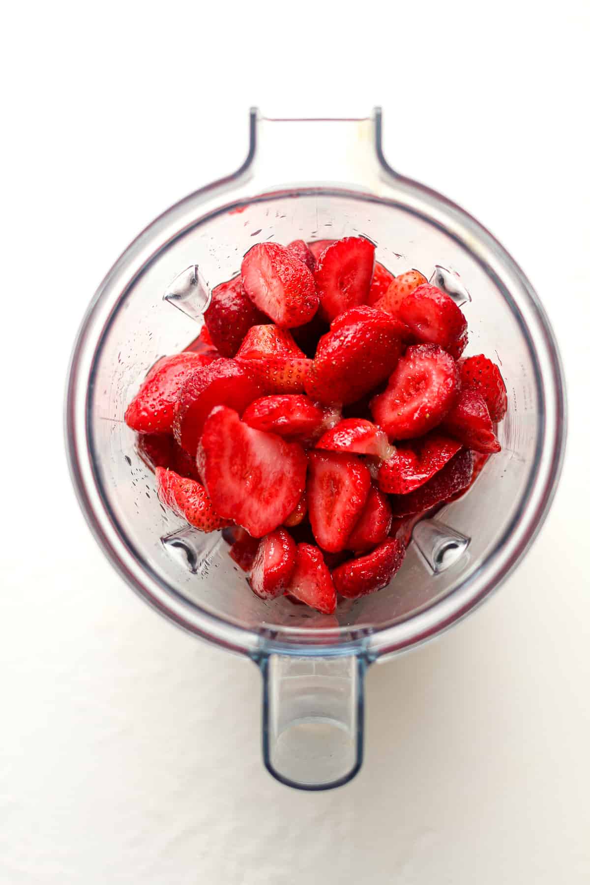 A blender full of strawberries and the liquid ingredients.