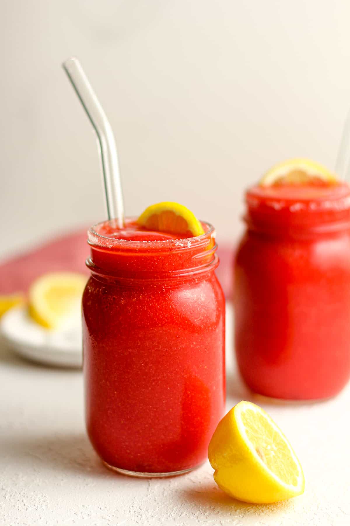 Side shot of two jars of bright red strawberry lemonade slushies.