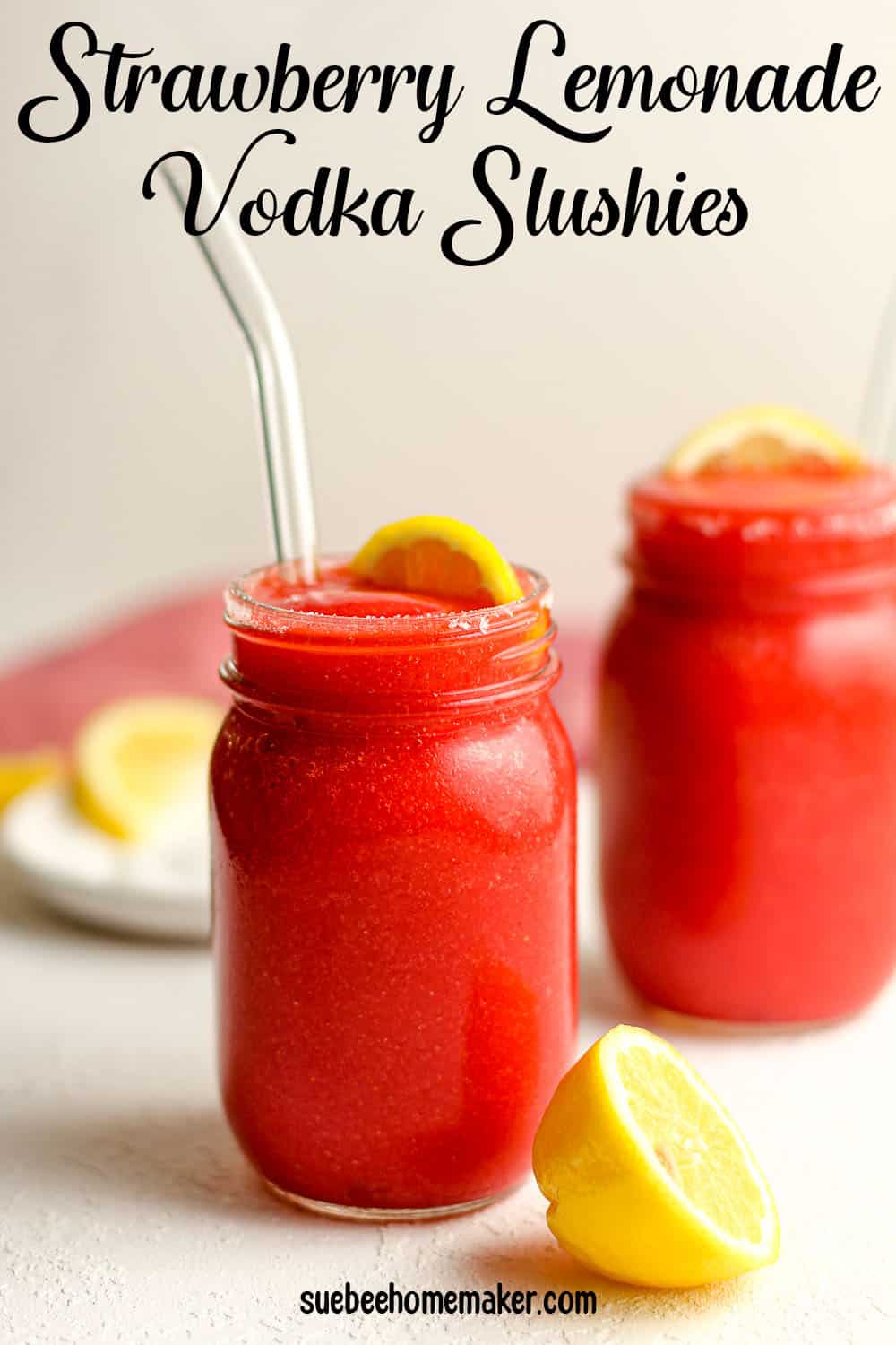 Two mason jars of strawberry lemonade vodka slushies, with lemon wedges