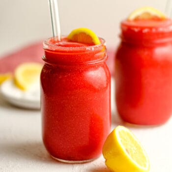 Two jars of strawberry lemonade vodka slushies, with glass straws.