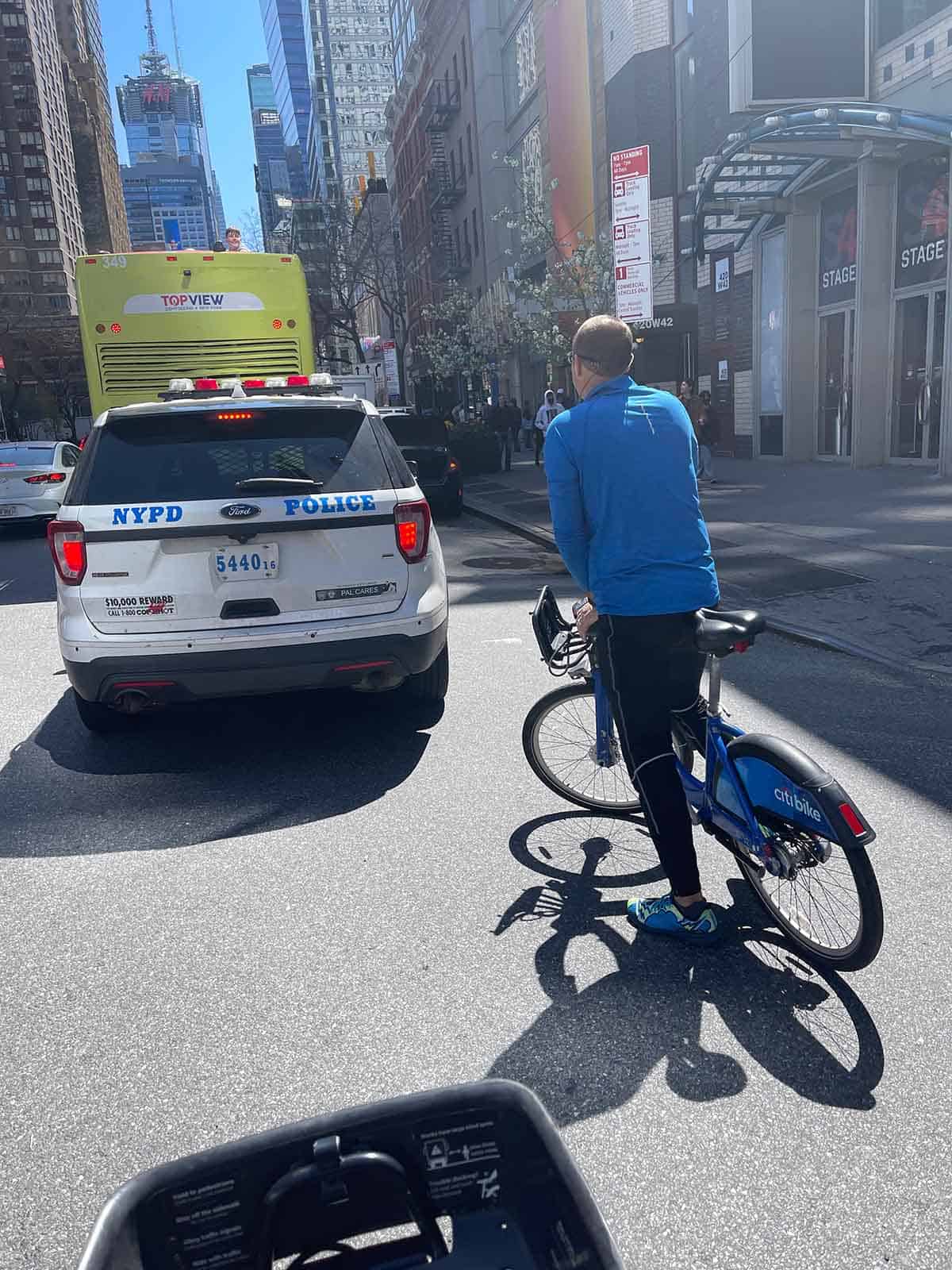Mike riding bike in back of NYPD car.