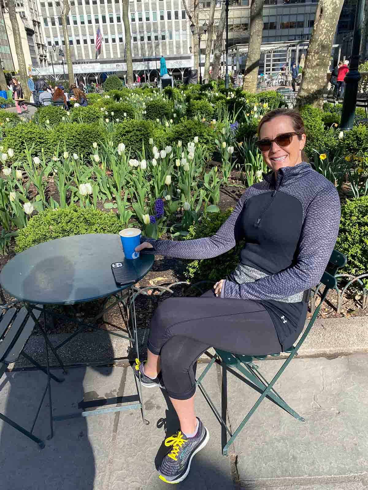 Sue sitting at a little table with a cup of coffee.