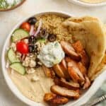 A chicken and hummus bowl with quinoa, tzatziki sauce, and veggies.
