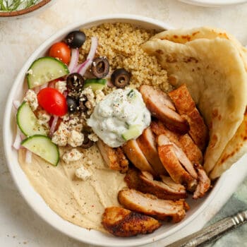 A bowl of chicken and hummus with quinoa and tzatziki sauce.
