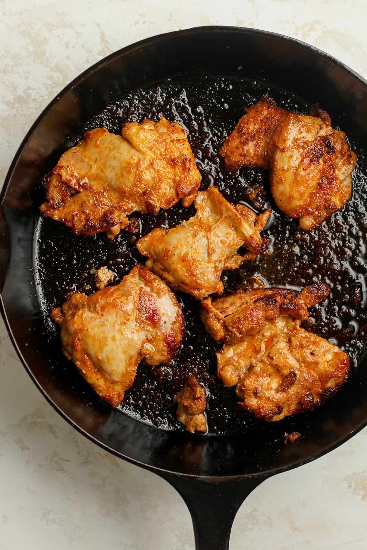 A skillet of seared chicken thighs.