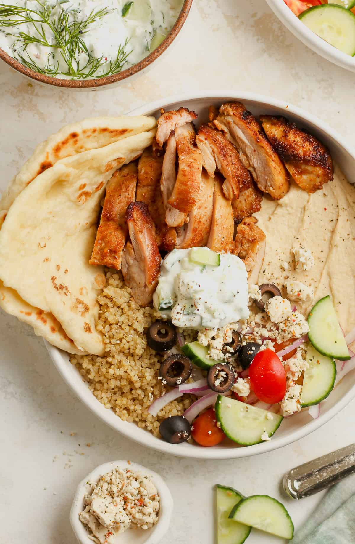 A closeup on a bowl of chicken and hummus bowls with naan bread and veggies.