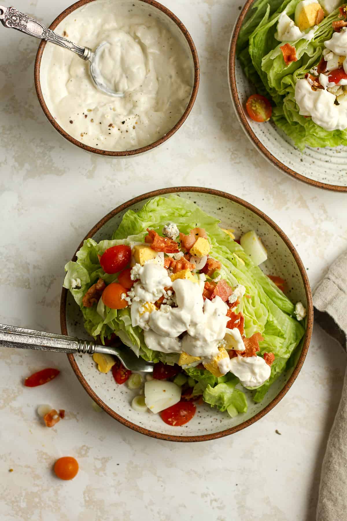 Two bowls of wedge salad with toppings and blue cheese dressing.