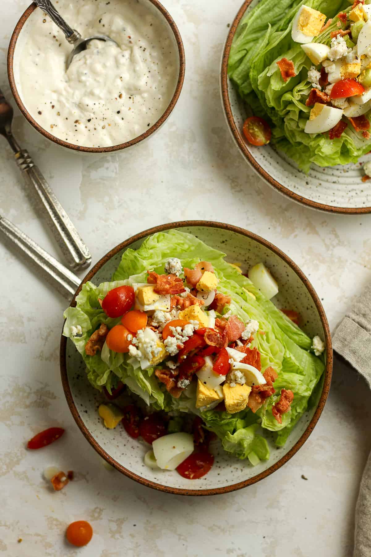 Two bowls of wedge salad with a bowl of dressing next to them.