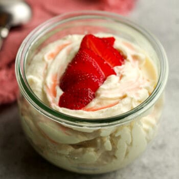 A jar of cream cheese fruit dip with sliced strawberries on top.