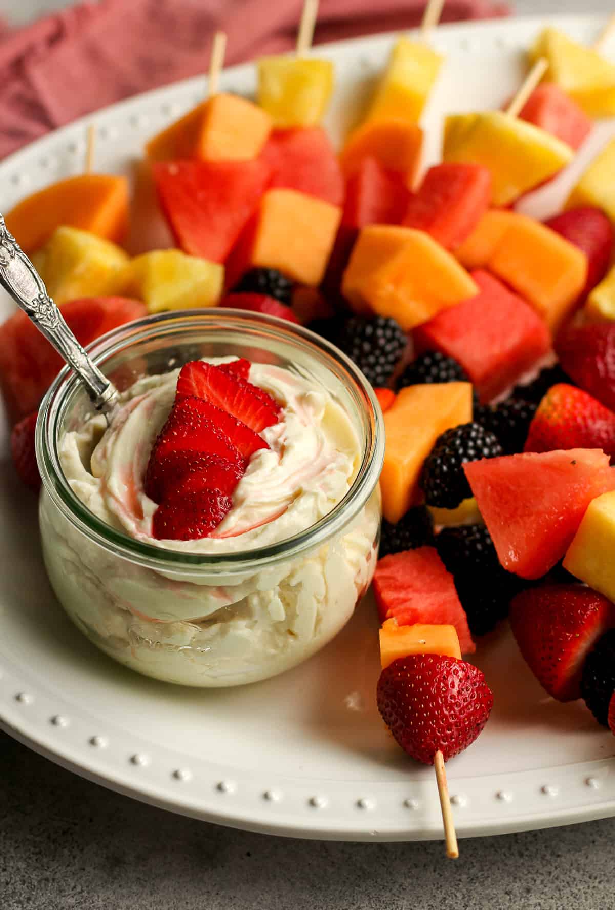 Side view of a platter of fruit with a jar of fruit dip.