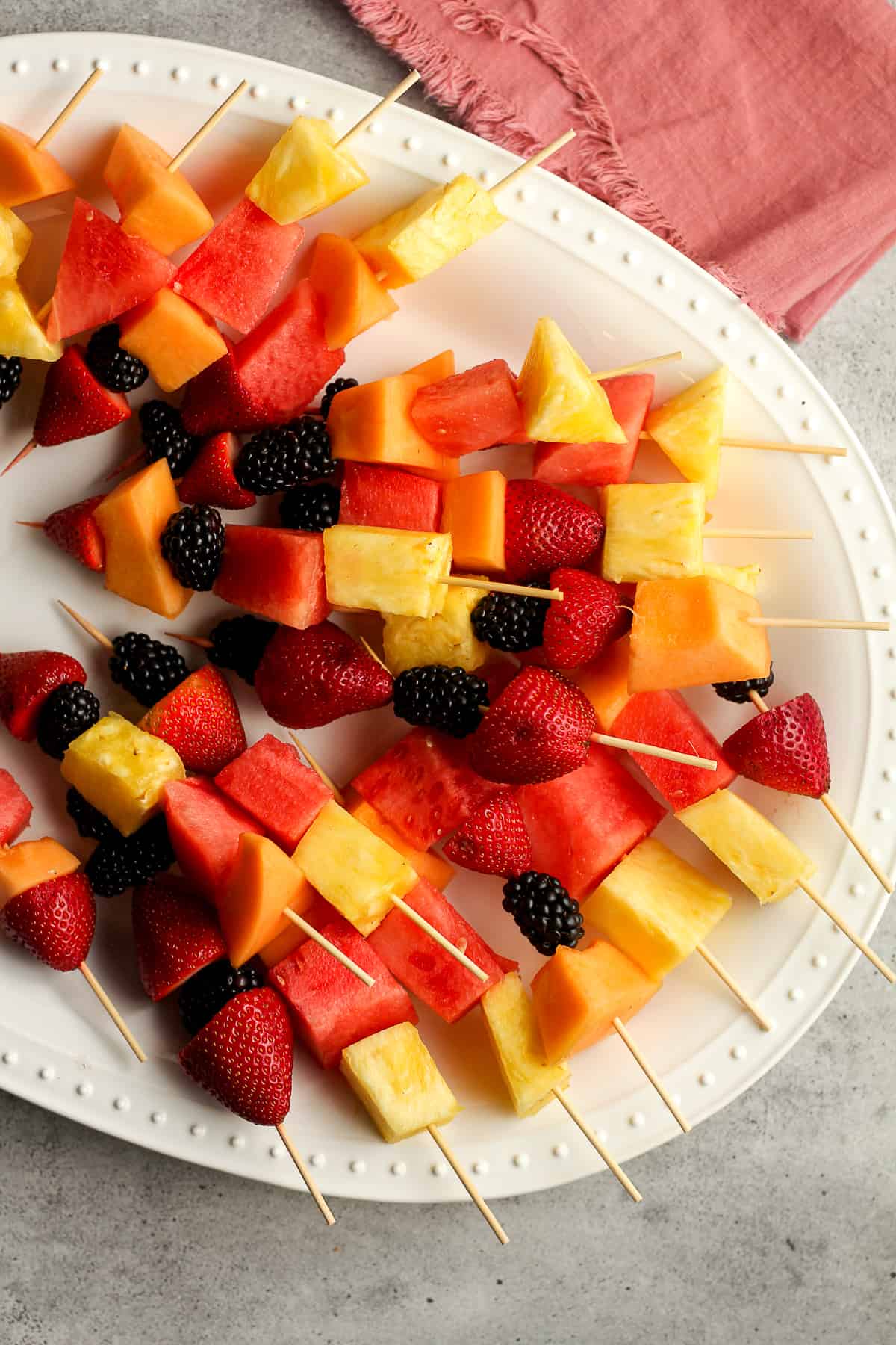 A platter of fruit kabobs with miscellaneous fruit.